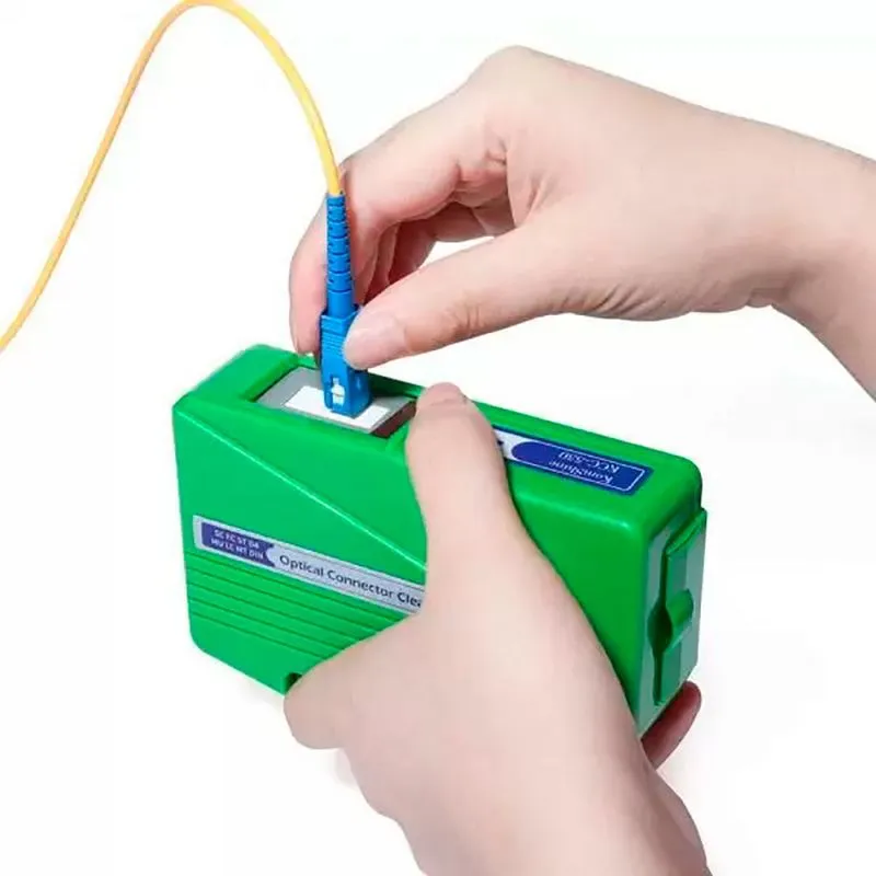 Pessoa utilizando limpador óptico de fibra para limpar conector SC azul. Equipamento verde para manutenção e limpeza de cabos de fibra óptica.